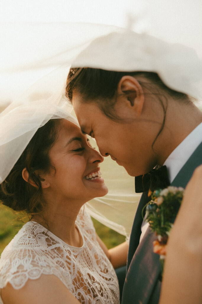 Bride and groom under a veil smiling, at their wedding at the Barn at Gibbet Hill