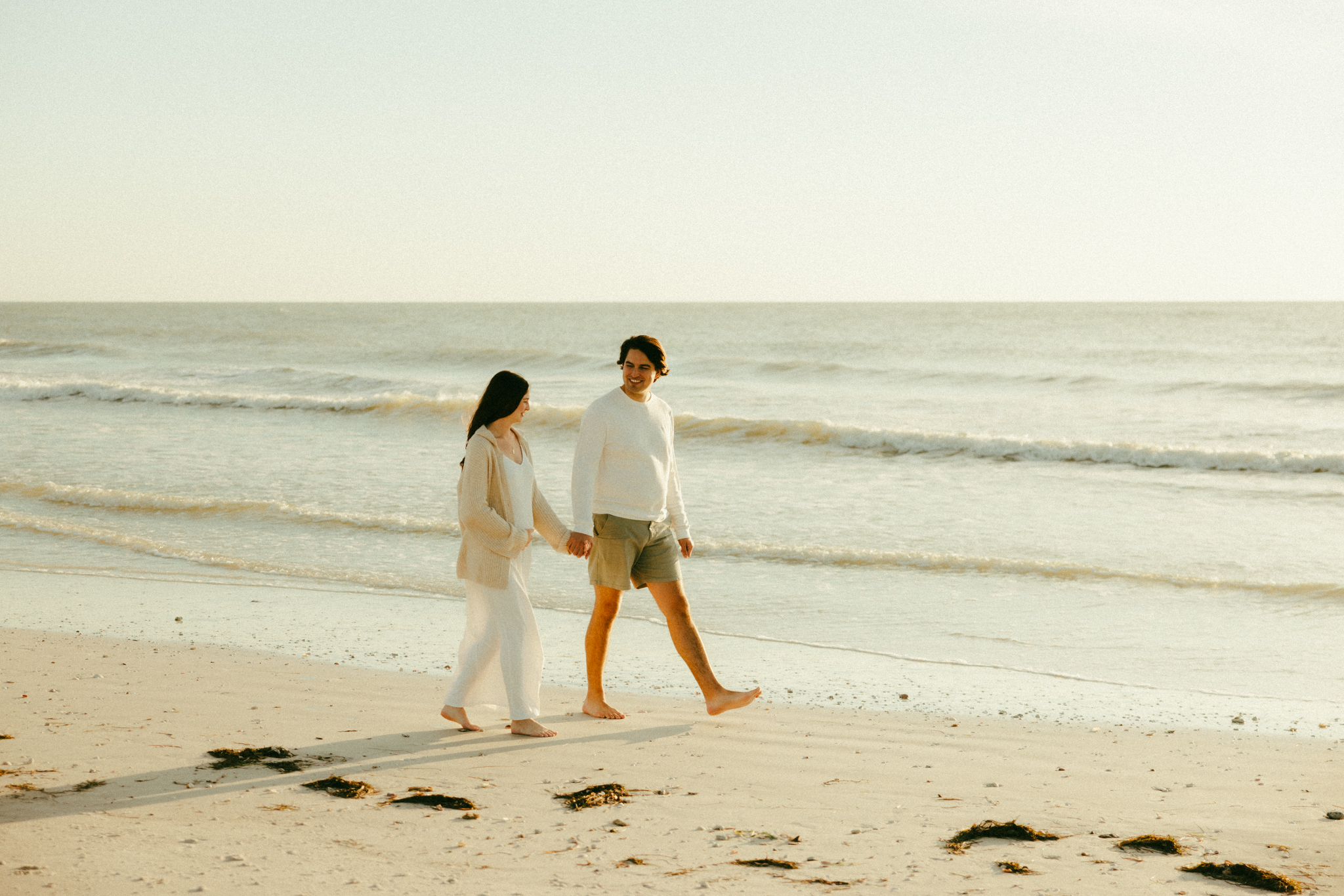 Maternity photo of couple walking along the shore of a Florida beach.
