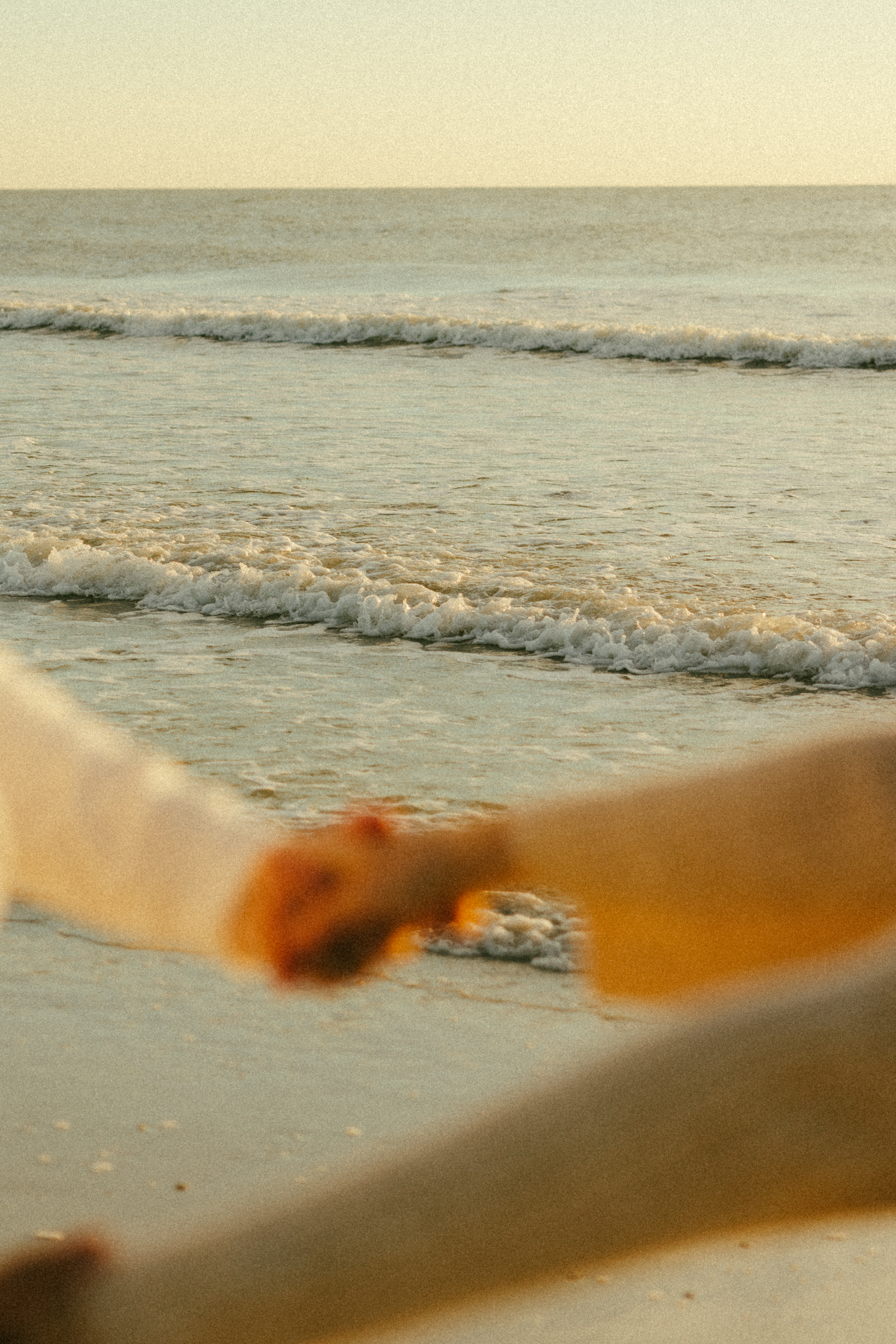 blurry hands in foreground with waves on the beach in focus. Documentary style photo
