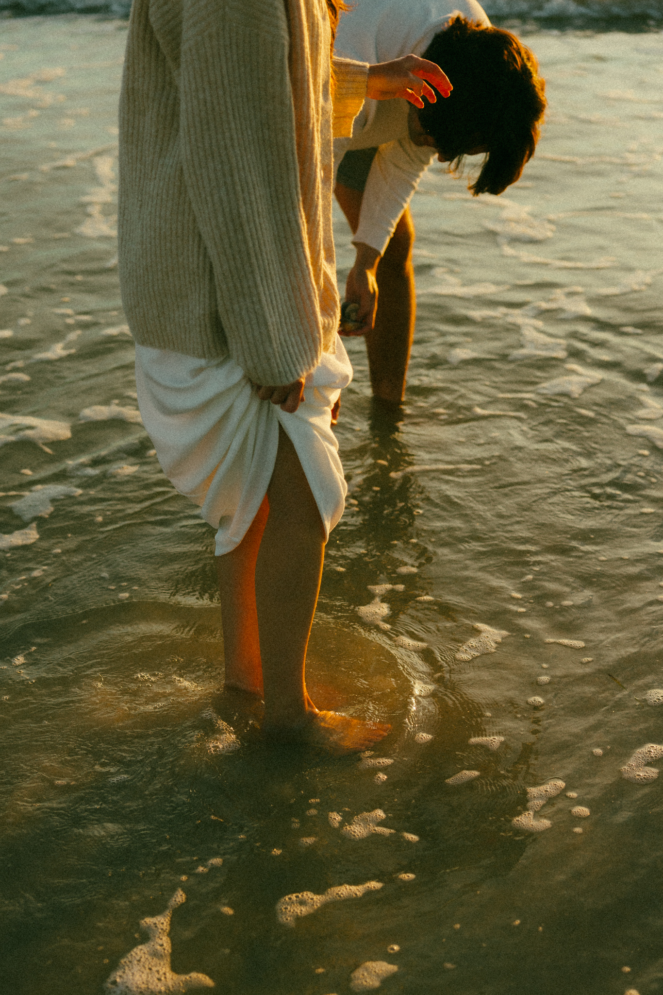 documentary style photo of couple's feet in the ocean as they look for sea shells.