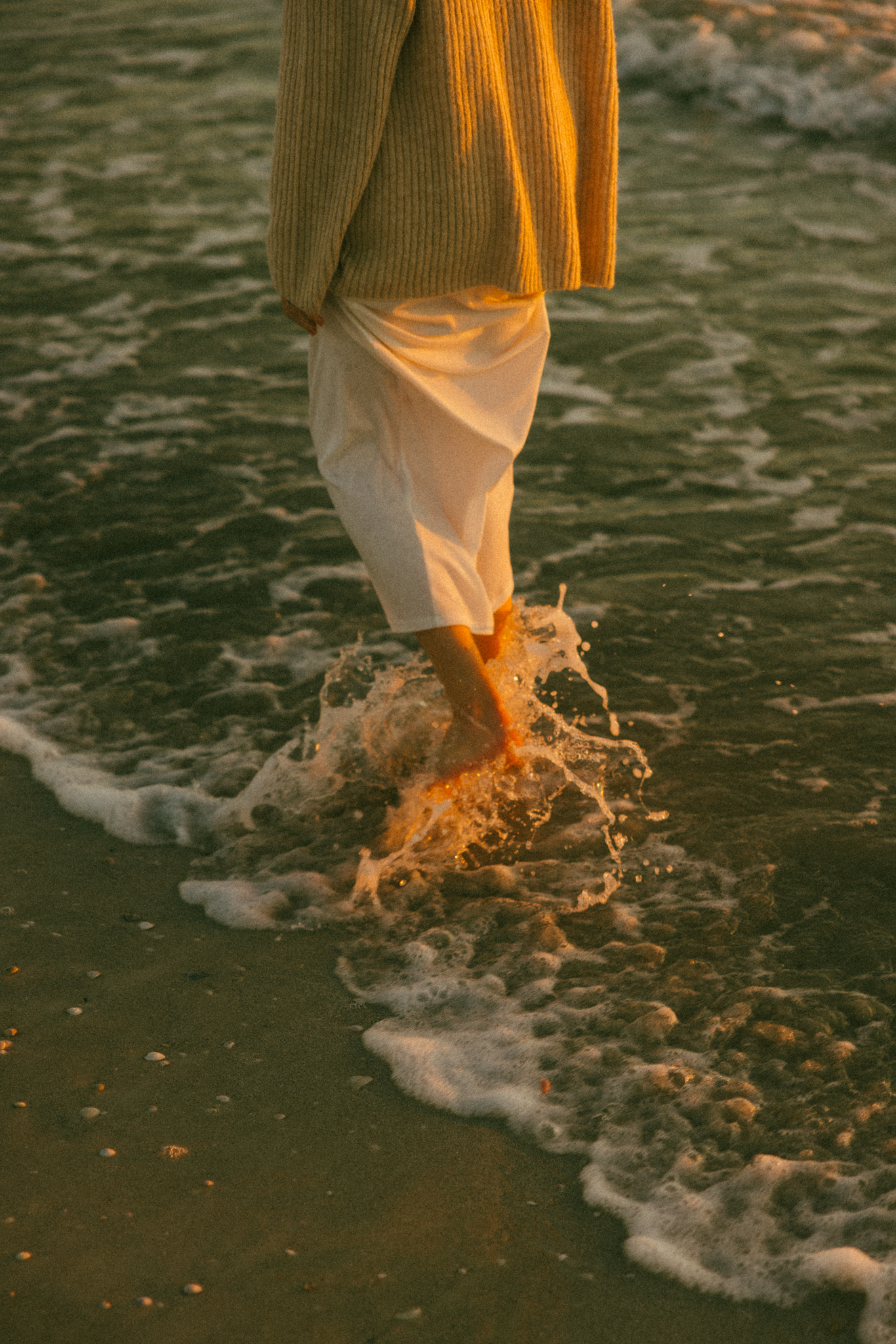 Golden sunlight hitting woman's feet as she walks through the water on Florida beach. Documentary photo session