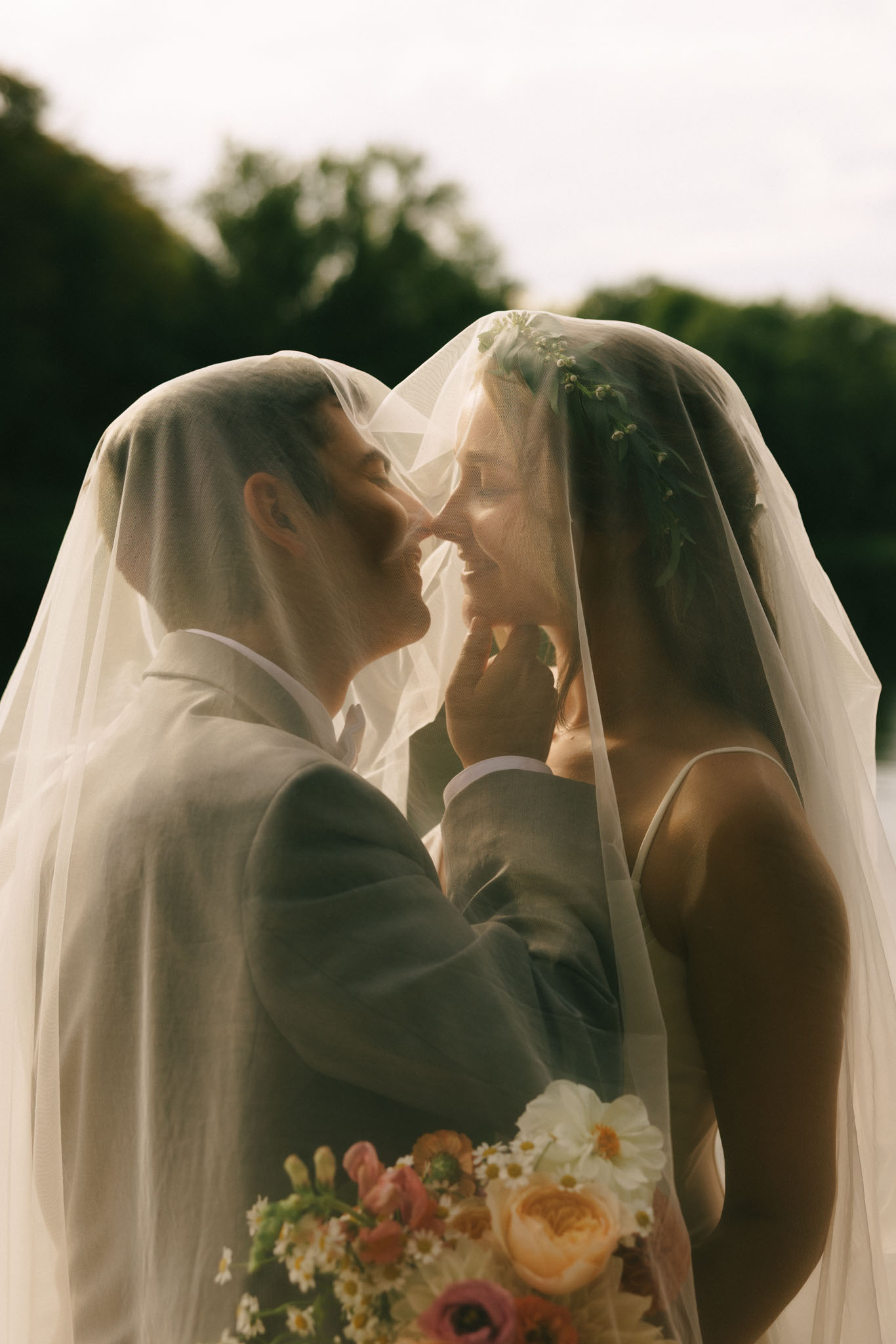 Bride and groom kiss under veil with soft warm light