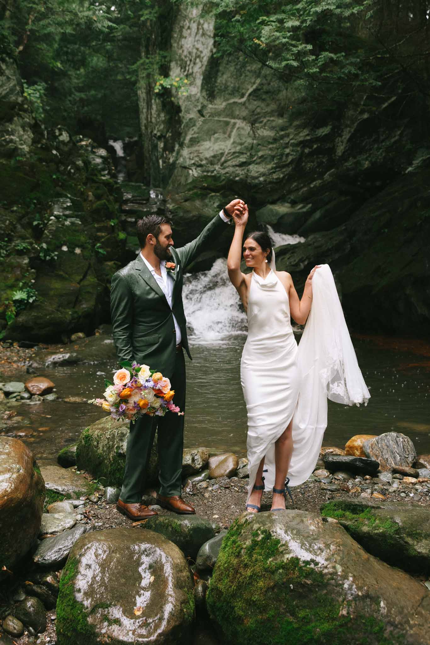 Bride and groom stand in front of Madbush Falls in Vermont
